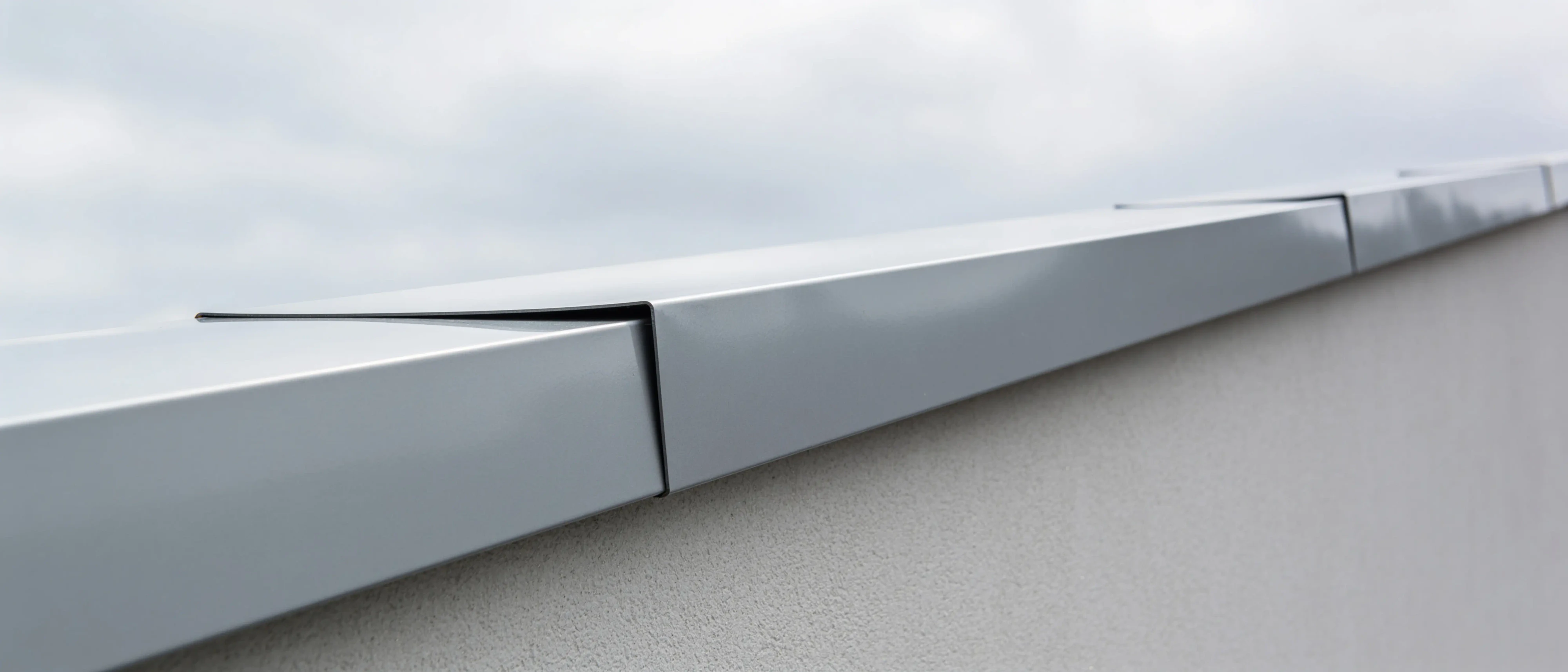 Mauerabdeckung aus hellgrau beschichtetem Aluminium auf einer Attika vor bedecktem Himmel
