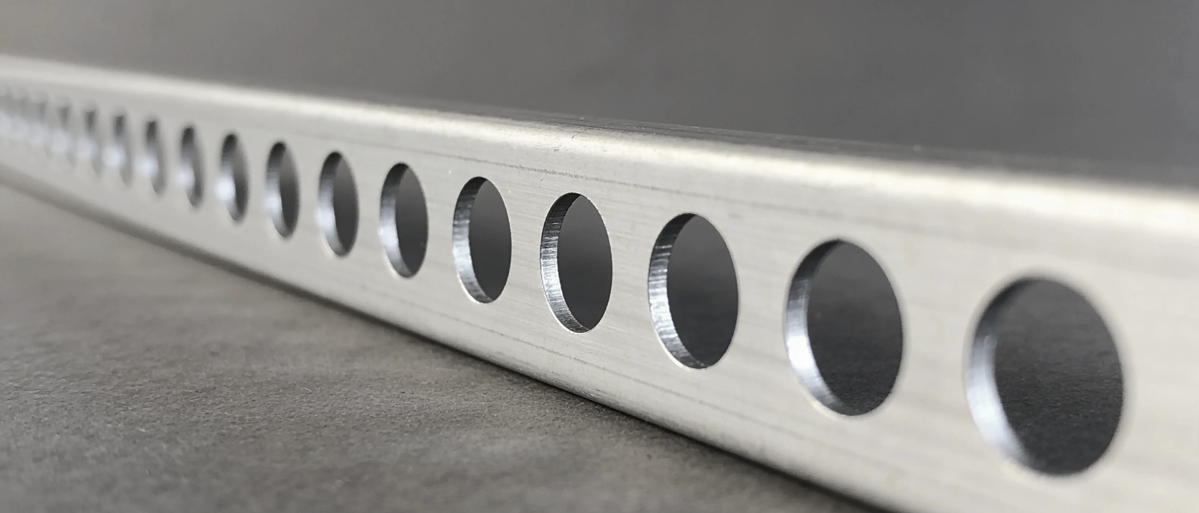Reihe gestanzter Rundlöcher in einem Schenkel aus blankem Aluminium
